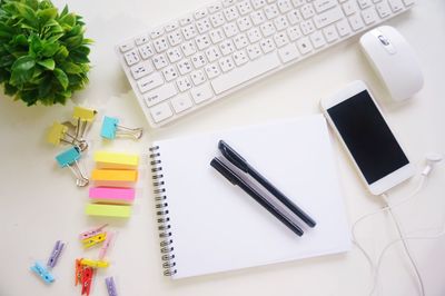 Directly above shot of technologies with note pad on white background