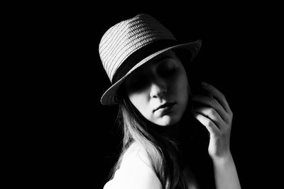 Side view of young woman wearing hat against black background