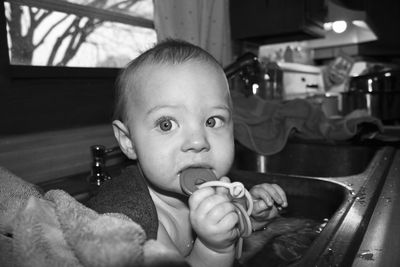 Cute toddler playing with toy while having bath in kitchen sink at home