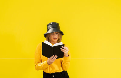 Close-up of a smiling young caucasian woman on a yellow background holding a book