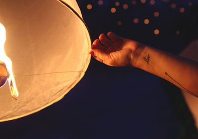 Cropped image of woman releasing paper lantern at night