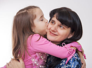 Cute daughter kissing on mother cheek against white background