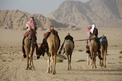 Rear view of people riding on camel in desert against mountain