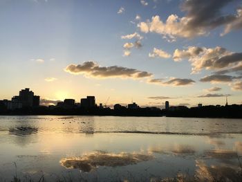 Scenic view of river by buildings against sky during sunset