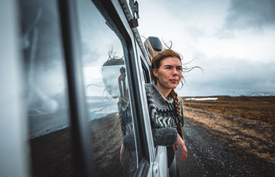 Portrait of young woman in car against sky