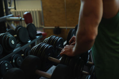 Midsection of muscular man standing by dumbbells in gym