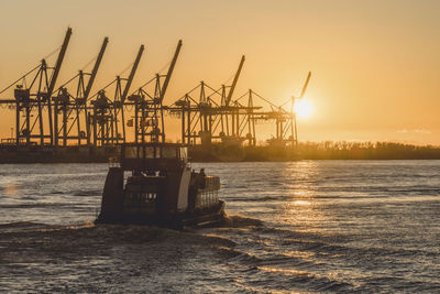 Cranes at commercial dock against sky during sunset