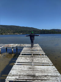 Rear view of man standing on pier over lake against sky