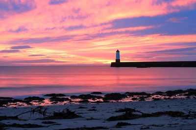 Lighthouse by sea against sky during sunset