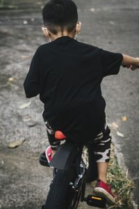 Rear view of boy riding bicycle on road