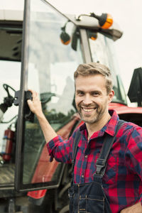 Portrait of smiling man standing by tractor at farm