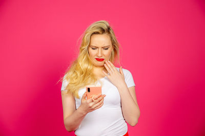 Young woman using smart phone against pink background