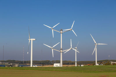 Windmills on field against clear blue sky