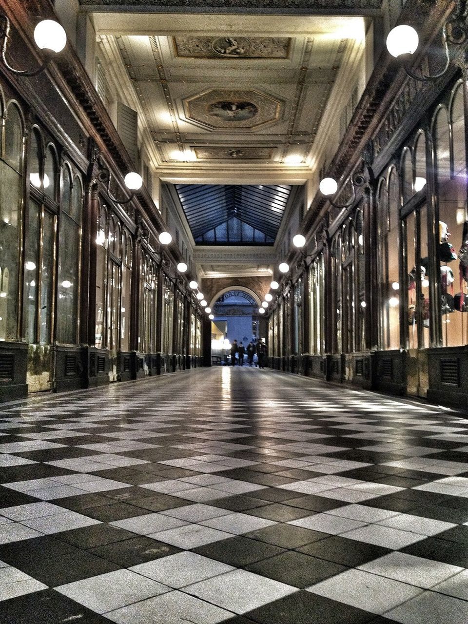 indoors, architecture, built structure, corridor, the way forward, ceiling, flooring, tiled floor, diminishing perspective, architectural column, empty, incidental people, in a row, illuminated, column, lighting equipment, city, colonnade, vanishing point, building