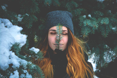 Young woman with eyes closed holding pine needles during winter