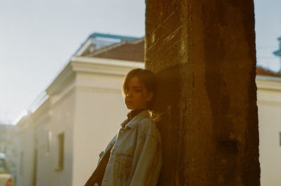 Portrait of young woman standing by building against sky