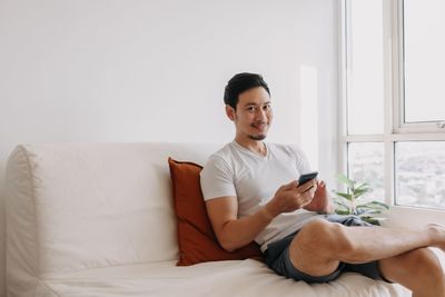 Young woman using mobile phone while sitting on bed at home