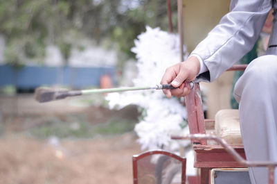 Midsection of man holding cane sitting on horse cart