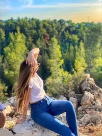 Rear view of woman sitting on rock against trees