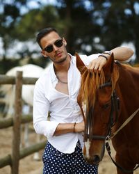 Man wearing sunglasses standing with horse outdoors
