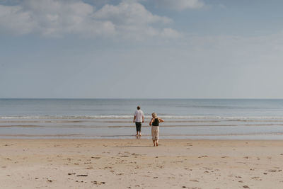 Rear view of woman walking at beach against sky