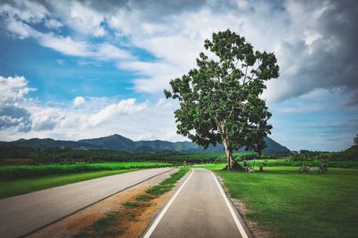 Road passing through field against cloudy sky