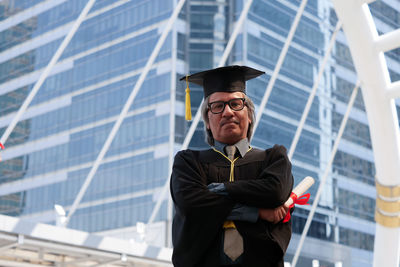 Portrait of businessman in graduation gown against office building