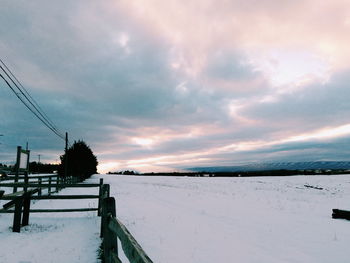 Snow covered landscape against sky during sunset