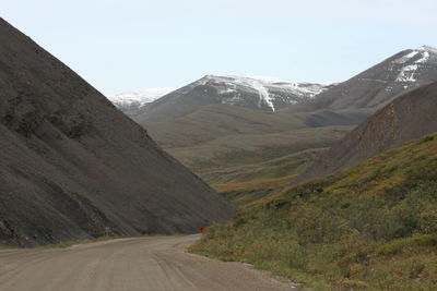 Road leading towards mountains against clear sky