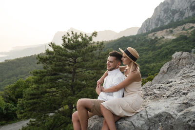 Young man sitting on rock against mountains