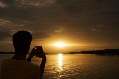 Rear view of man photographing at sunset