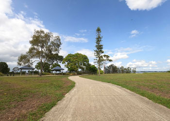 Road amidst field and trees against sky