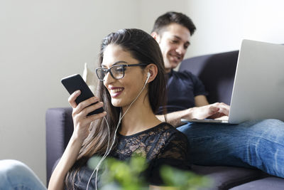 Young woman on the phone in the living room with boyfriend on the couch in the background