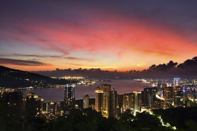 Illuminated modern buildings in city against sky at sunset