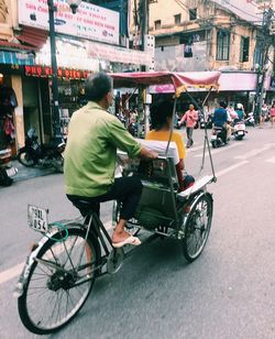 Rear view of people riding bicycle on city street