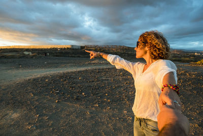 Woman standing on land against sky during sunset