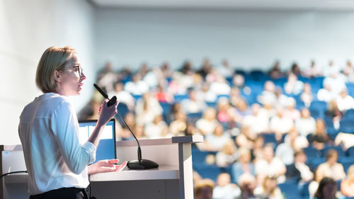 Female speaker giving a talk on corporate business conference. unrecognizable people in audience at