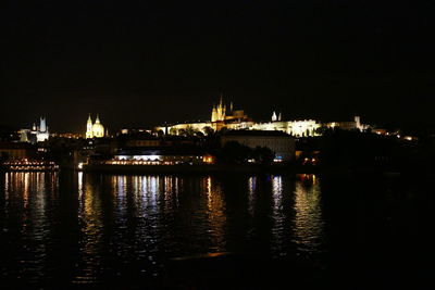 Illuminated city by river against sky at night