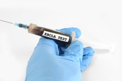 Cropped hand of doctor wearing surgical glove holding syringe over white background