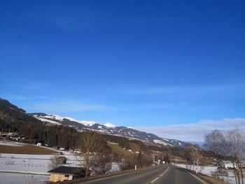 Road amidst snowcapped mountains against blue sky