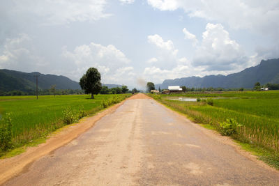 Empty road amidst field against sky