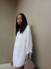 Portrait of young woman standing by wall