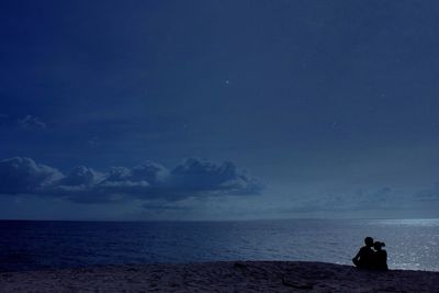 Silhouette man sitting on beach against sky at night