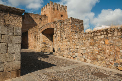 Stone wall of old building against cloudy sky