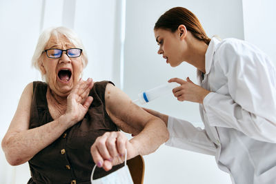 Senior woman and doctor making faces during vaccination at hospital