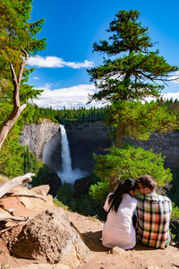 People sitting on rocks by plants against sky