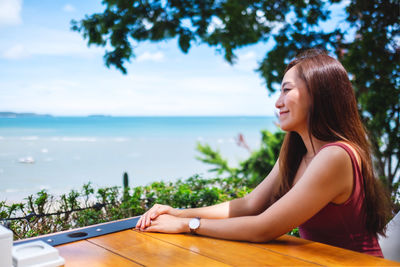 Side view of young woman using mobile phone by sea