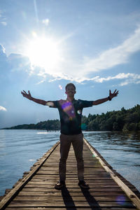 Full length of man with arms outstretched standing on pier against sky