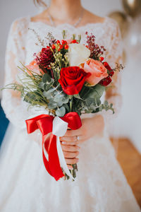 Midsection of woman holding bouquet against red wall