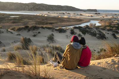 Couple wearing knit hat sitting together on sand dune during sunset